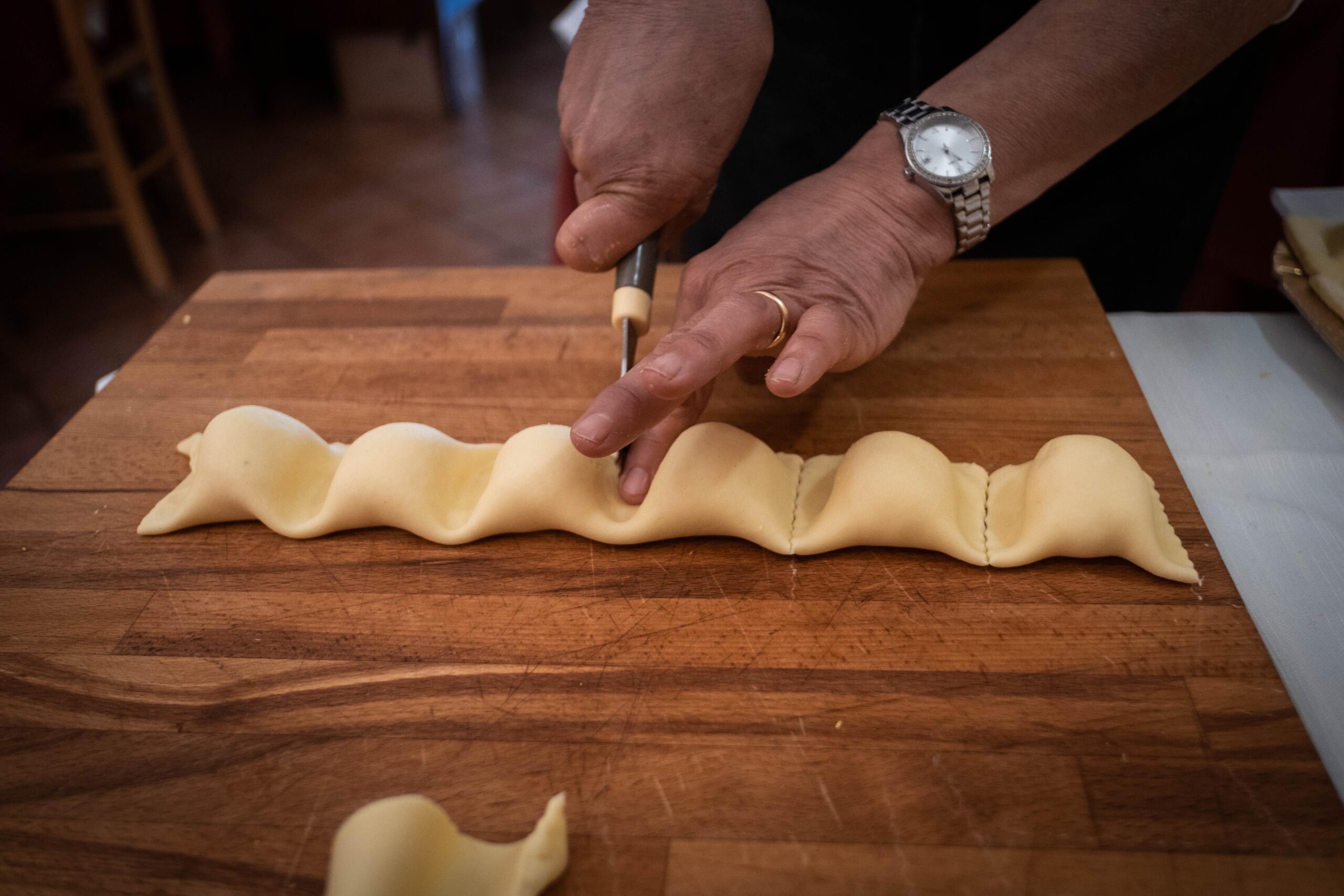 Mani di una persona tagliano dei ravioli freschi